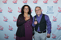 Vor einer weißen Wand mit mehreren SpaceNet Awards-Logos stehen ein Mann und eine Frau