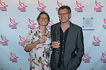 Vor einer weißen Wand mit mehreren SpaceNet Awards-Logos stehen ein Mann und eine Frau