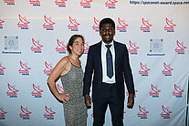 Vor einer weißen Wand mit mehreren SpaceNet Awards-Logos stehen ein Mann und eine Frau