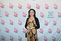 Vor einer weißen Wand mit mehreren SpaceNet Awards-Logos steht eine Frau im Kleid
