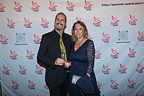 Vor einer weißen Wand mit mehreren SpaceNet Awards-Logos stehen ein Mann und eine Frau