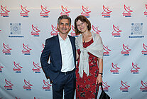 Vor einer weißen Wand mit mehreren SpaceNet Awards-Logos stehen ein Mann im Anzug und eine Frau im Kleid