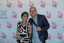 Ein Mann und eine Frau stehen vor einer weißen Wand, die mit mehreren SpaceNet Award Logos bedeckt ist