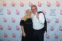 Vor einer weißen Wand mit mehreren SpaceNet Awards-Logos stehen ein Mann im Anzug und eine Frau im Kleid