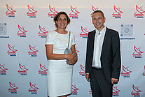 Vor einer weißen Wand mit mehreren SpaceNet Awards-Logos stehen ein Mann im Anzug und eine Frau im Kleid