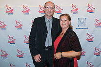 Vor einer weißen Wand mit mehreren SpaceNet Awards-Logos stehen ein Mann und eine Frau