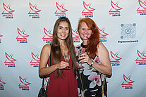 Zwei Frauen in Kleidern stehen vor einer Wand, auf der mehrere SpaceNet Award-Logos zu sehen sind