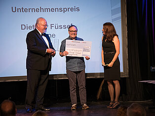 Sebastian Von Bomhard und Katja Holzer übergeben den Unternehmenspreis an einen Mann auf der Bühne