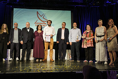 Mehrere Personen stehen auf einer Bühne, und im Hintergrund ist das SpaceNet Award Logo zu sehen