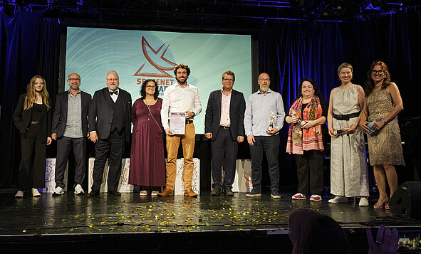 Mehrere Personen stehen auf einer Bühne, und im Hintergrund ist das SpaceNet Award Logo zu sehen