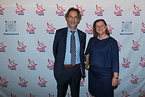Vor einer weißen Wand mit mehreren SpaceNet Awards-Logos stehen ein Mann und eine Frau