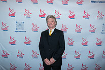 Vor einer weißen Wand mit mehreren SpaceNet Awards-Logos steht ein Mann im Anzug