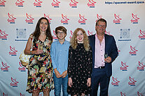 Vor einer weißen Wand mit mehreren SpaceNet Awards-Logos stehen zwei Erwachsene und zwei Kinder