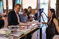 Mehrere Personen stehen an einem Tisch, der mit Büchern bedeckt ist