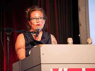 Eine Frau hält eine Rede vor einem Rednerpult und einem Mikrofon